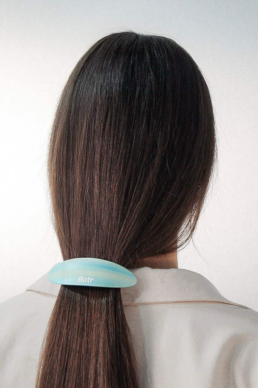 A person shown from the back wearing a  blue butr barrette with the brand name 'Butr' printed on it, set against a plain light gray background.